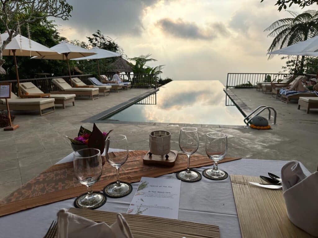 Poolside dining table set with wine glasses at Munduk Moding Plantation Bali overlooking infinity pool at sunset