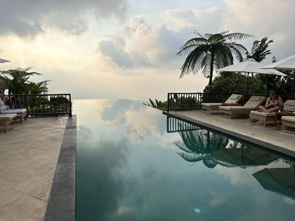 Munduk Moding Plantation Bali infinity pool at dusk with dramatic sky reflected in still water and loungers along edge