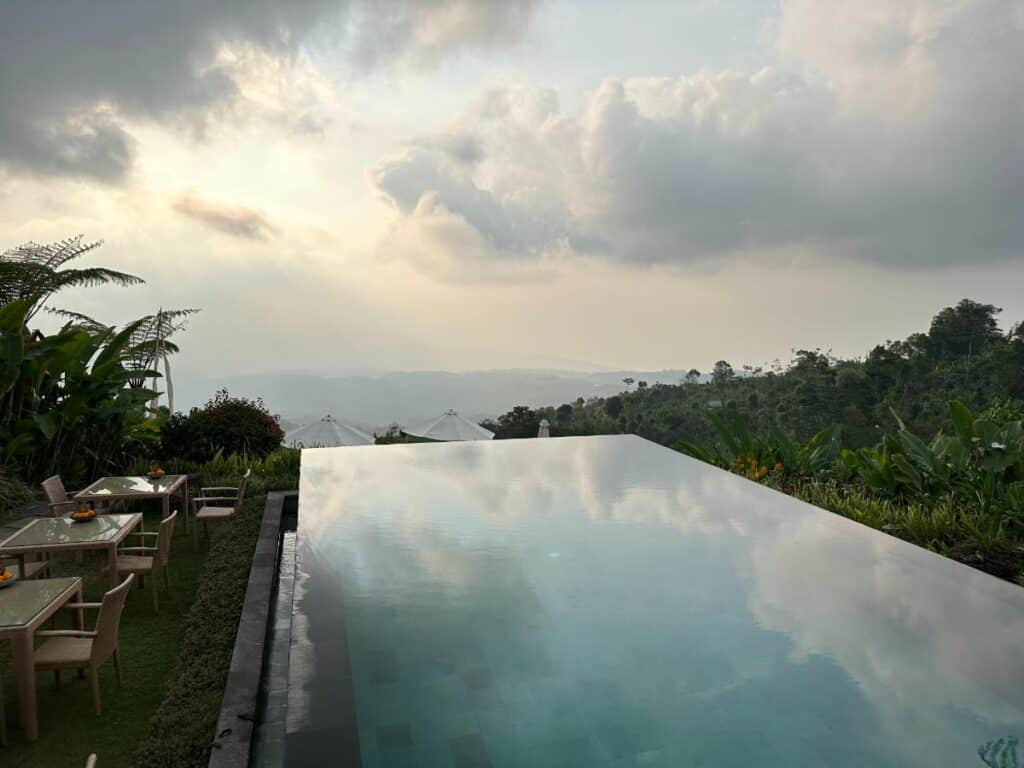 Water-level view of Munduk Moding Plantation Bali infinity pool with sunlit sky and distant highland plateau beyond