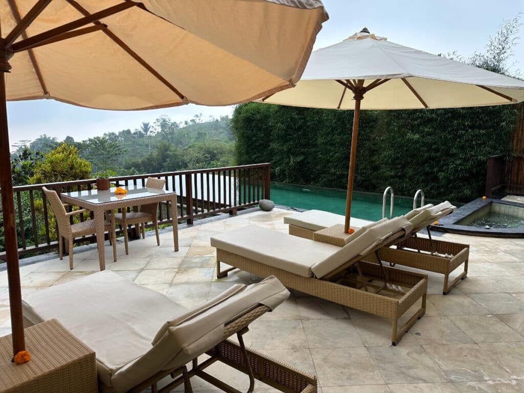Resort terrace with sun loungers, parasols and green pool at Munduk Moding Plantation Bali amid tropical nature surroundings