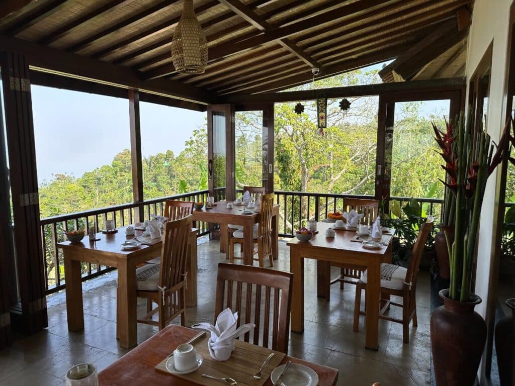 Open-air dining lounge at Munduk Moding Plantation Bali with teak tables and chairs overlooking the tropical highland canopy