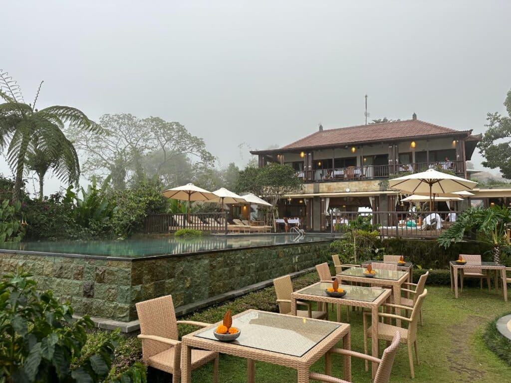 Munduk Moding Plantation Bali main building and pool shrouded in morning mist with tropical trees in the foreground
