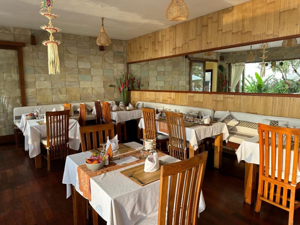 Restaurant dining room interior at Munduk Moding Plantation Bali with banquette seating, white tablecloths and wooden chairs
