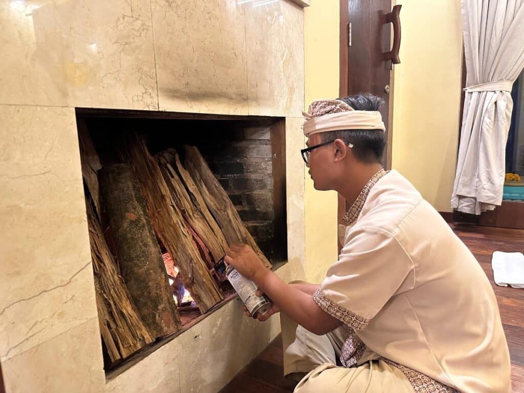 Balinese staff member in traditional Balinese udeng headwear stacking logs to light the villa fireplace at Munduk Moding Plantation