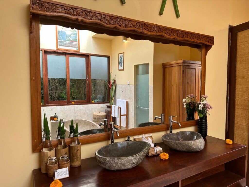 Double hand-carved stone basin sinks with ornate wooden mirror frame in Munduk Moding Plantation Bali villa bathroom