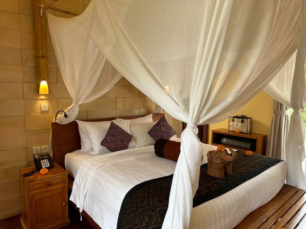 Front view of king canopy bed with white linen and purple cushions in Munduk Moding Plantation Bali villa bedroom