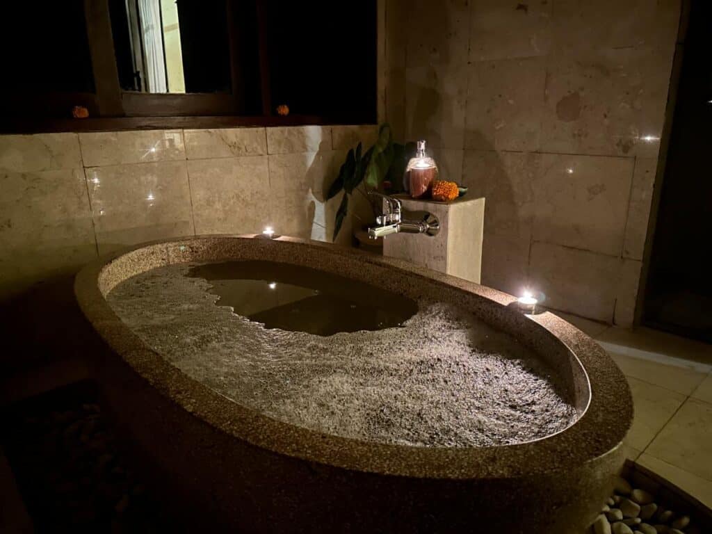Carved volcanic stone bathtub with warm evening accent lighting in Munduk Moding Plantation Bali villa bathroom