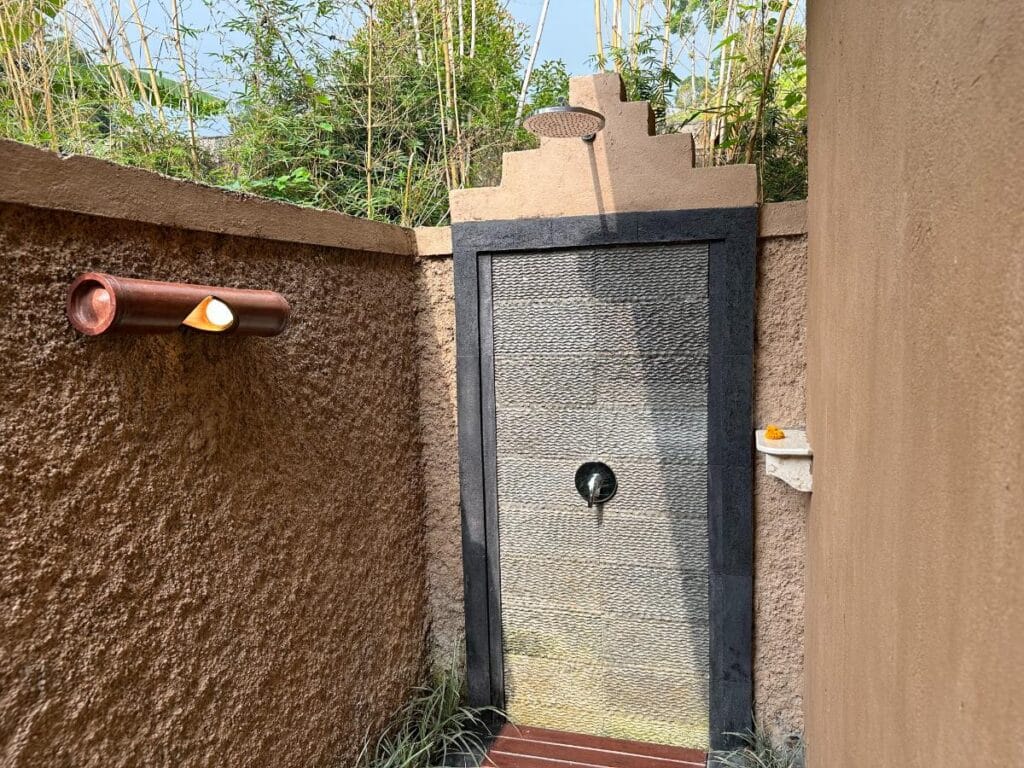 Outdoor stone-walled rain shower at Munduk Moding Plantation Bali villa with tropical garden views and natural lighting