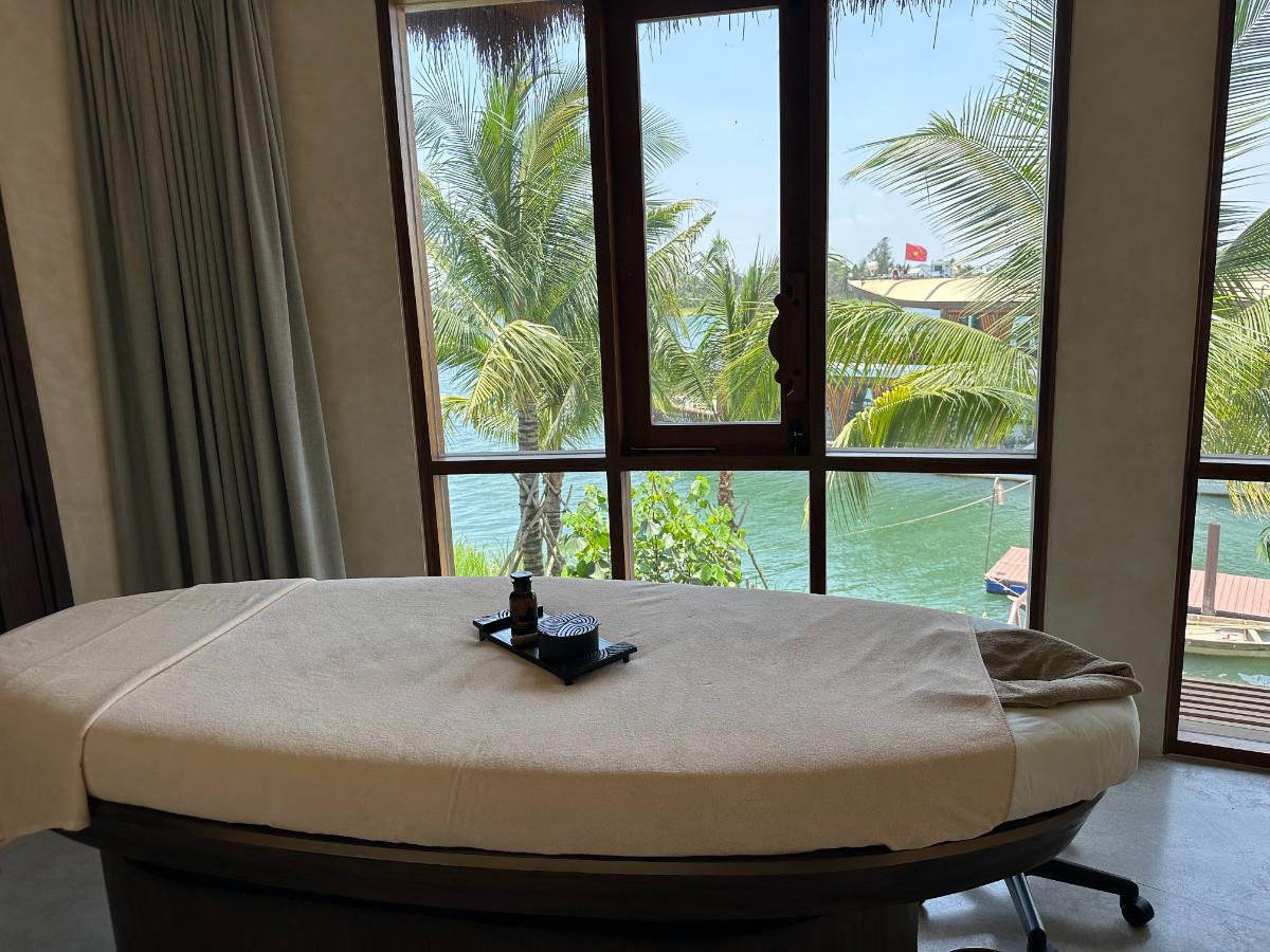 Spa-Entspannungsliege mit Blick auf die raumhohen Fenster des Thu Bon Flusses, Namia River Retreat, Hoi An, Vietnam