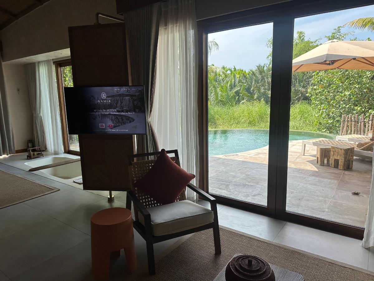 Wohnzimmer mit drehbarer TV-Trennwand und Glaswand mit Poolblick, Pool-Villa, Namia River Retreat, Hoi An, Vietnam