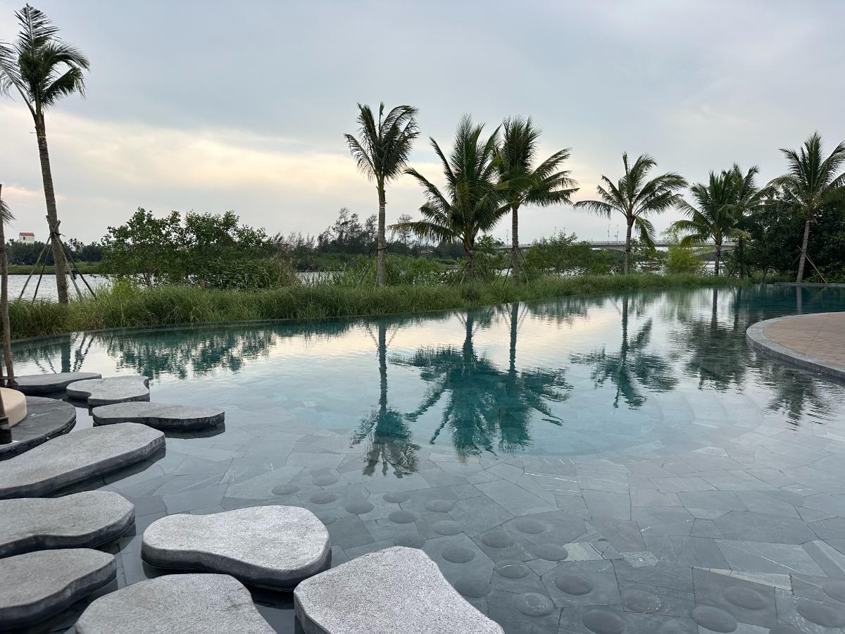 Infinity-Pool mit Steintrittstellen und Palmenreflexionen in der Abenddämmerung, Namia River Retreat, Hoi An, Vietnam