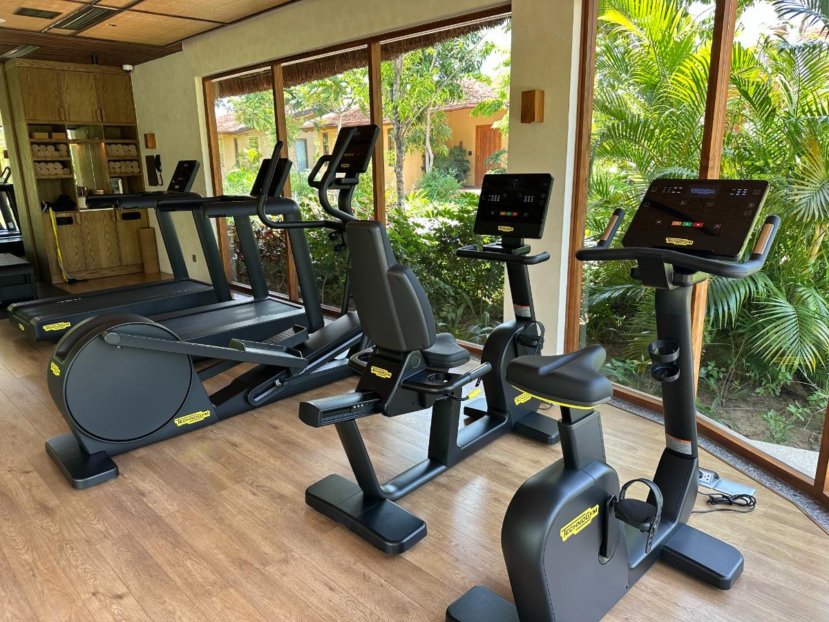 Laufband und Heimtrainer am Fenster des Fitnessstudios mit Blick auf den Garten, Namia River Retreat, Hoi An, Vietnam
