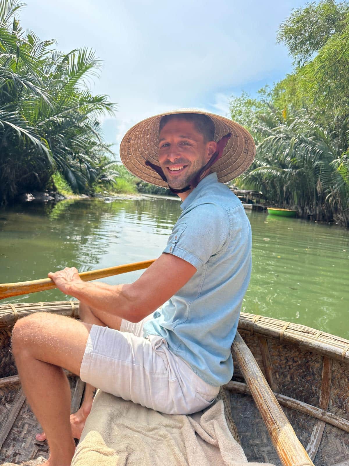 Paddeln in einem Bambuskorbboot auf dem Fluss mit einem konischen Hut, Namia River Retreat, Hoi An, Vietnam